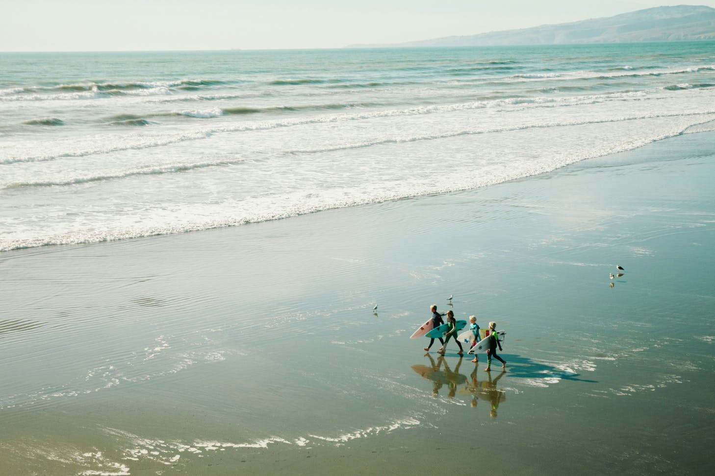Kids walk out across Sarborough Beach in Sumner to go surfing.